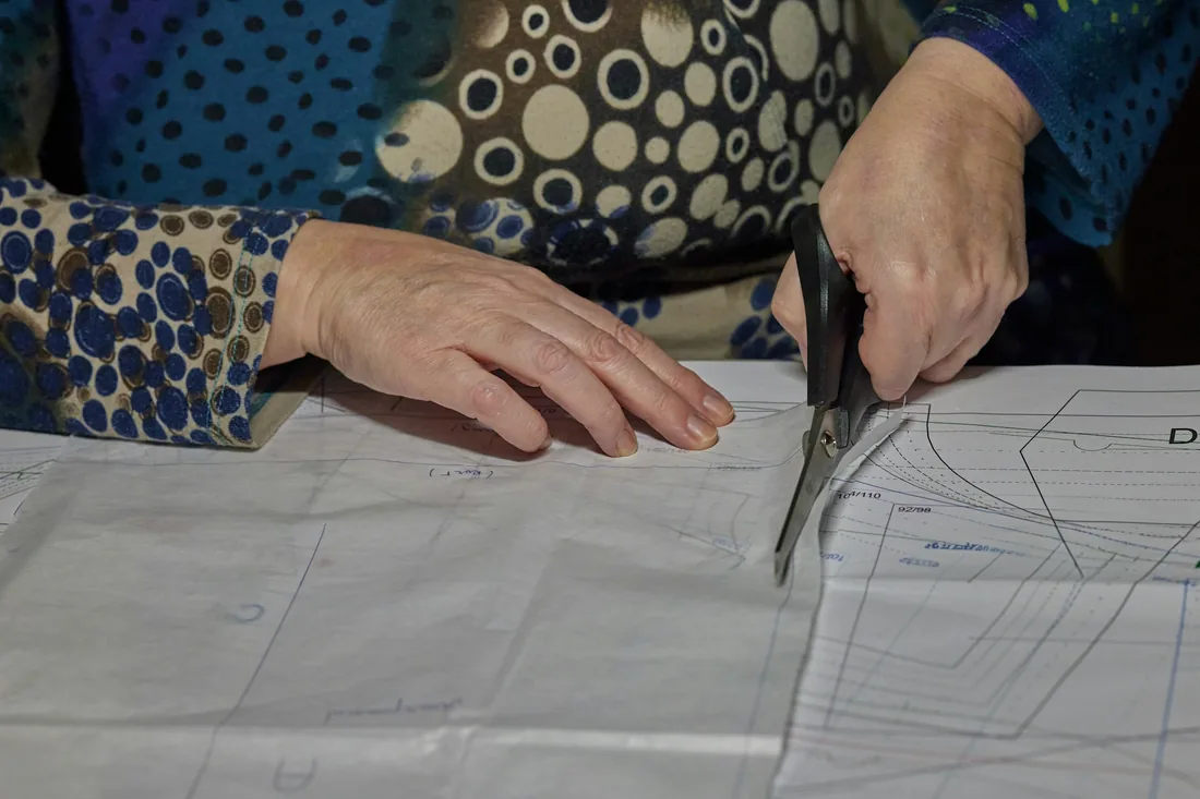 Manos recortando con tijeras las piezas de un patrón dibujado sobre papel, encima de la mesa de corte de un taller de vestuario.
